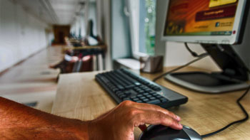 ręka trzymająca myszkę obok klawiatury i ekranu komputera